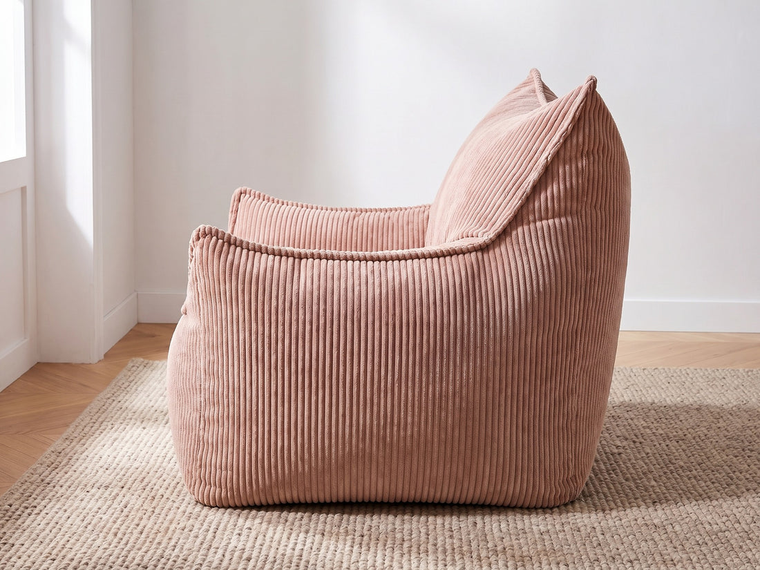 Pouf fauteuil en velours côtelé rose poudré vu de profil sur un tapis beige dans un salon lumineux