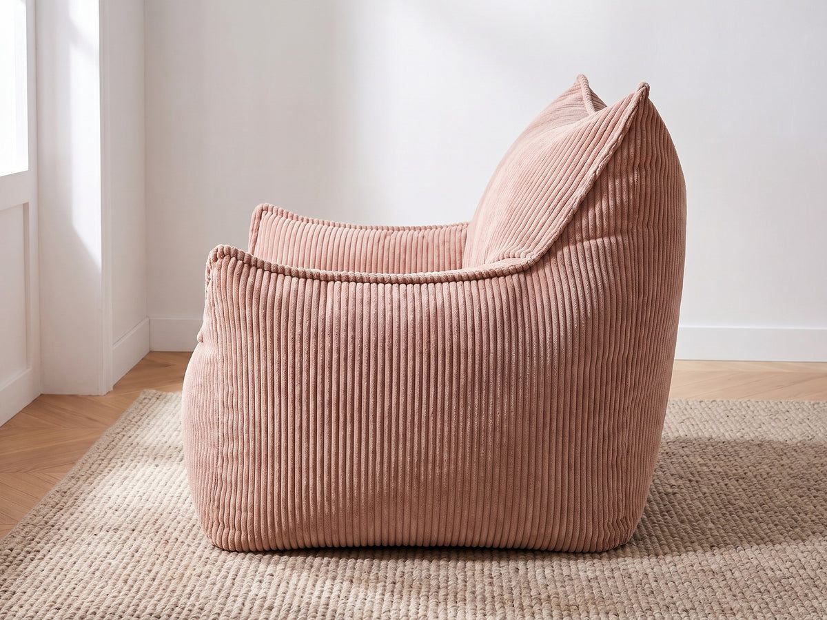 Pouf fauteuil en velours côtelé rose poudré vu de profil sur un tapis beige dans un salon lumineux